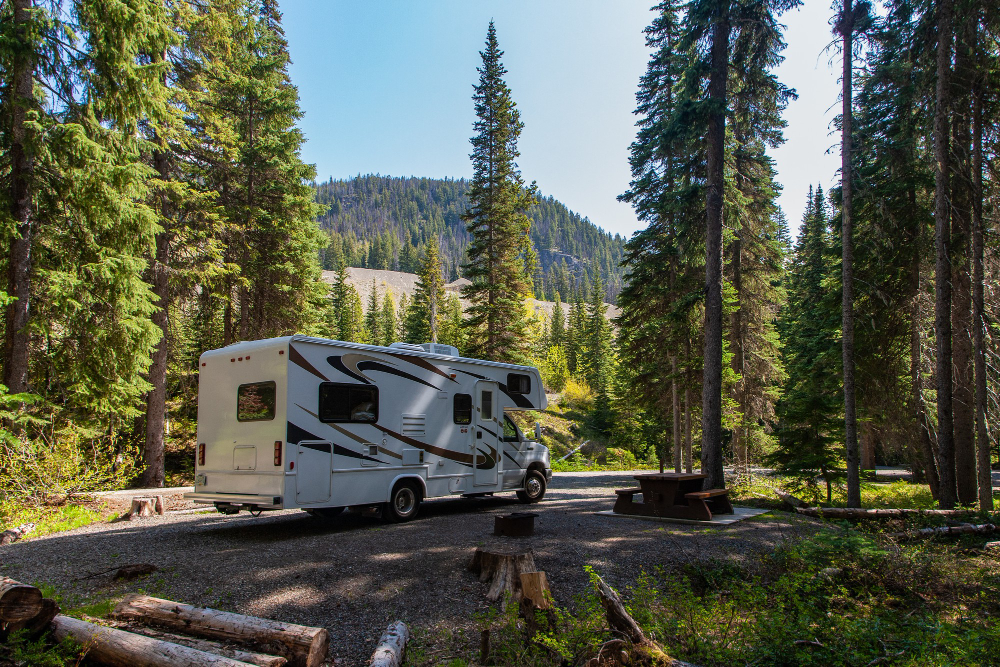 A campsite in the mountains with an RV and a wooden bench